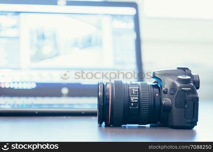 Professional camera with telephoto lens on a table, laptop in the blurry background