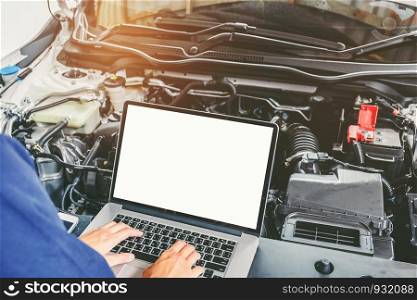 Professional car mechanic working in auto repair service using laptop bon car