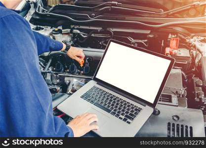 Professional car mechanic working in auto repair service using laptop on car