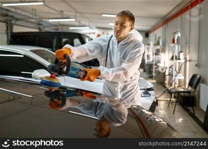 Professional car service male worker with orbital polisher polishing freshly painted surface. Professional car service worker polishing painted surface