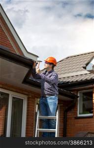 Professional carpenter standing on high ladder and repairing house roof