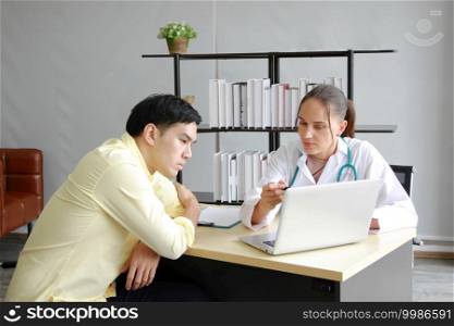 Professional Caucasian Female Psychiatrist is counseling and researching on website with laptop for treatment asian man at clinic office. Major depressive disorder patients and healthcare Concept. 