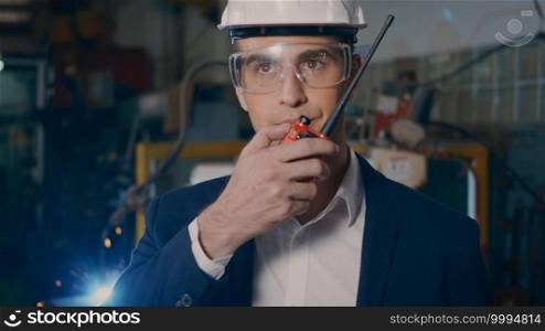 Professional confident engineer businessman in suits safety hats and goggles stand holding walkie-talkie in an heavy industrial facility manufacturing with a steel welding from robot with fire spark