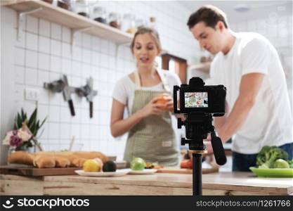 Professional digital mirrorless camera recording video blog of happy caucasian couple cooking in the kitchen room, Camera for photographer or video and live streaming concept,Vlogger and blogger.