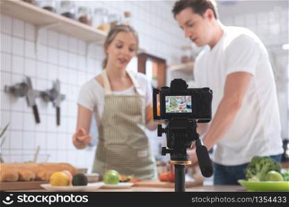Professional digital mirrorless camera recording video blog of happy caucasian couple cooking in the kitchen room, Camera for photographer or video and live streaming concept,Vlogger and blogger.