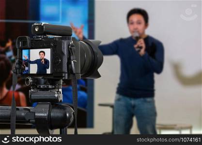 Professional digital Mirrorless camera with microphone on the tripod recording video blog of asian Speaker on the stage seminar, Camera for photographer or Video and Technology Live Streaming concept