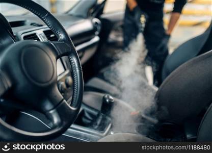Professional dry cleaning of car salon with steam cleaner. Carwash service, vehicle salon hygiene, male worker removes dirt and dust. Cleaning of car salon with steam cleaner