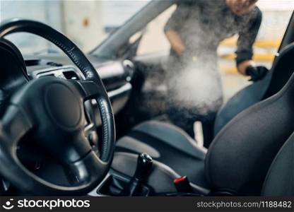 Professional dry cleaning of car salon with steam cleaner. Carwash service, vehicle salon hygiene, male worker removes dirt and dust