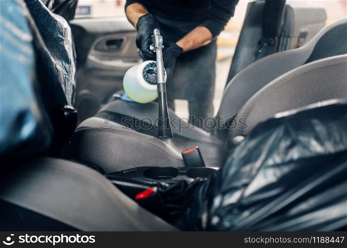 Professional dry cleaning of car seats. Carwash service, male worker in gloves using spray. Professional dry cleaning of car seats
