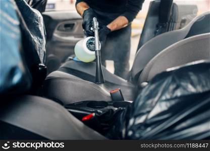 Professional dry cleaning of car seats. Carwash service, male worker in gloves using spray. Professional dry cleaning of car seats