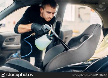 Professional dry cleaning of car seats. Carwash service, male worker using spray. Professional dry cleaning of car seats