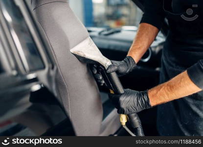 Professional dry cleaning of car seats with vacuum cleaner. Carwash service, male worker in gloves removes dust