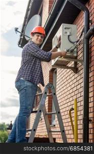 Professional electrician repairing air conditioner on outer wall of building