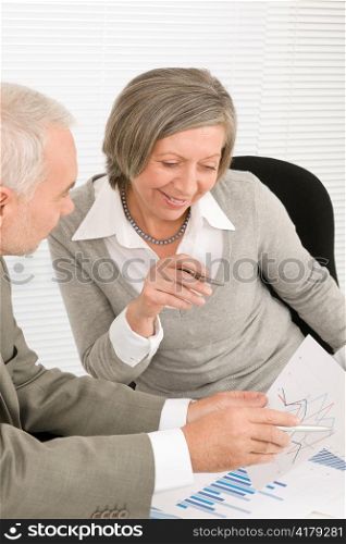 Professional elegant happy senior businesswoman looking graphs with man colleague