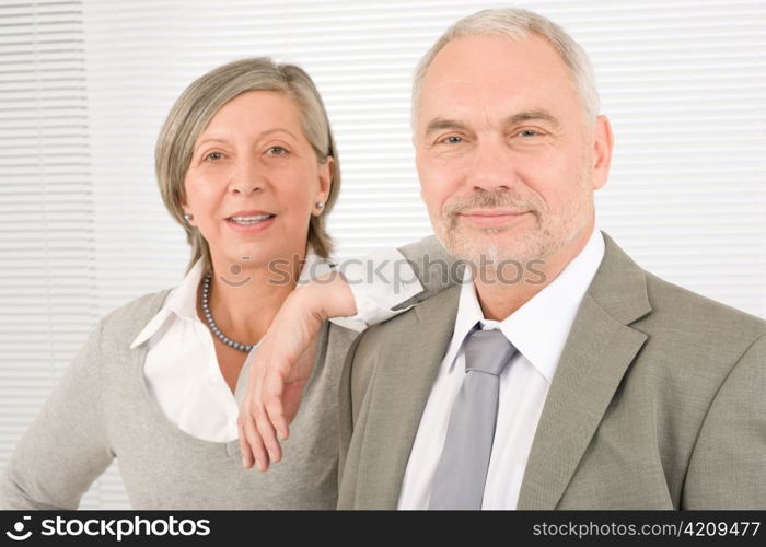 Professional elegant smiling senior businesswoman leaning against her male colleague