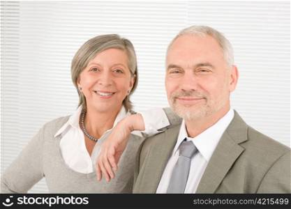 Professional elegant smiling senior businesswoman leaning against her male colleague