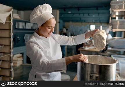 Professional female confectioner wearing white uniform putting flour into big metal bowl standing near table in confectionery. Female confectioner wearing white uniform putting flour into big metal bowl