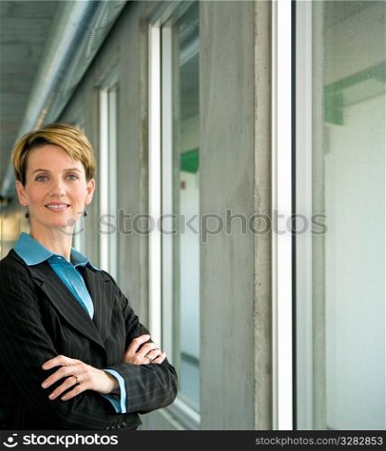 Professional female executive folding arms while standing in hallway.