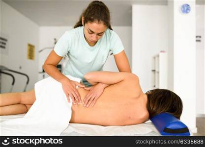 Professional female physiotherapist giving lumbar shoulder massage to brunette woman in hospital. Medical check at the shoulder in a physiotherapy center.
