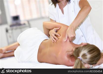 Professional female physiotherapist giving shoulder massage to blonde woman in hospital. Medical check at the shoulder in a physiotherapy center.