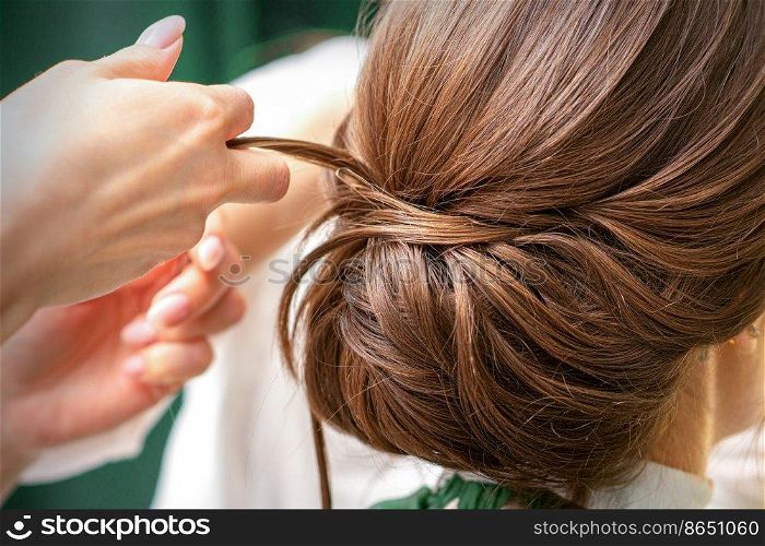 Professional hairdresser doing hairstyle for a beautiful brunette young woman with long hair. Concept of fashion and beauty. Professional hairdresser doing hairstyle for a beautiful brunette young woman with long hair. Concept of fashion and beauty.