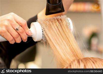 Professional hairdresser dry hair with a hairdryer and round hairbrush in a beauty salon. Professional hairdresser dry hair with a hairdryer and round hairbrush in a beauty salon.