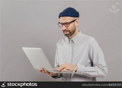 Professional IT developer downloads files, chats online in social networks, bloggs and surfes internet webpages wears formal shirt, stands against grey background. Technology and people concept
