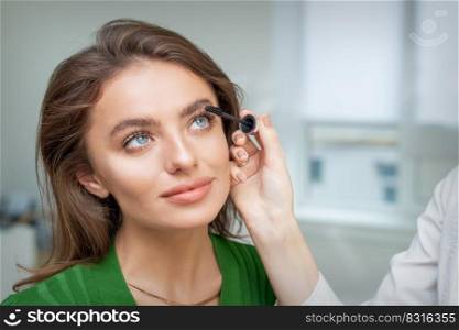 Professional makeup artist applying mascara on lashes of beautiful young caucasian woman in beauty salon. Makeup artist applying mascara on lashes
