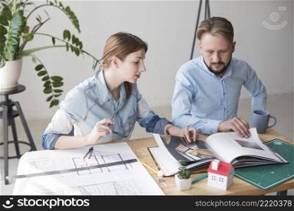 professional male female architect looking catalog while working office