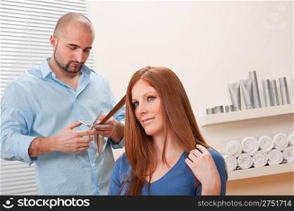 Professional male hairdresser cut with scissors at salon, female red hair customer getting new haircut