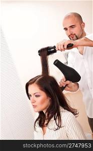 Professional male hairdresser with hair dryer and hair brush at salon with female customer