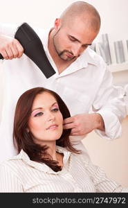 Professional male hairdresser with hair dryer at salon with female customer