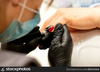 Professional manicure. A manicurist is painting the female nails of a client with red nail polish in a beauty salon, close up. Beauty industry concept. Professional manicure. A manicurist is painting the female nails of a client with red nail polish in a beauty salon, close up. Beauty industry concept.
