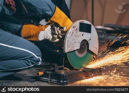 Professional mechanic man is cutting steel metal with rotating carbon blade cutter. Steel industry and workshop concept.