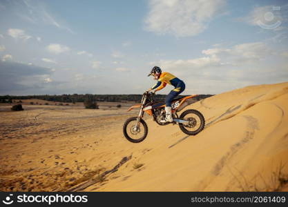 Professional motocross rider on helmet and protective suit sliding down sand hill. Speed moto racing in desert. Professional motocross rider sliding down sand hill