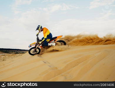 Professional motocross rider on helmet and protective suit sliding down sand hill. Speed moto racing. Professional motocross rider sliding down sand hill