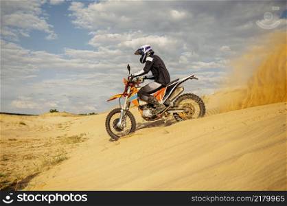 Professional motocross rider on helmet and protective suit sliding down sand hill. Speed moto racing. Professional motocross rider sliding down sand hill