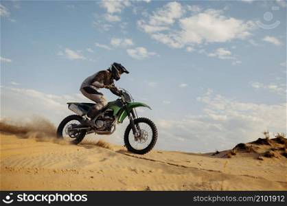 Professional motocross rider on helmet and protective suit sliding down sand hills. Speed moto racing in the desert. Professional motocross rider sliding down sand hill