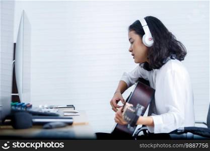 Professional musician young Asian woman vocalist Wearing Headphones plays guitar recording a song in digital studio at home,music production technology concept