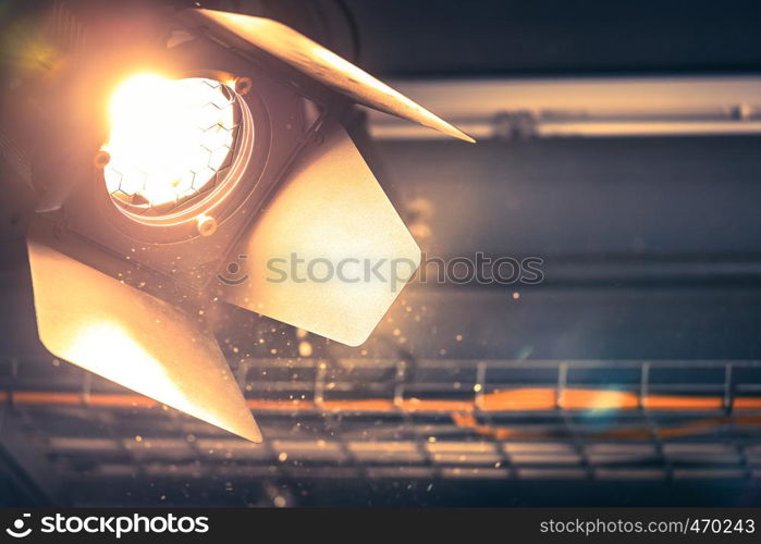 Professional orange studio spotlight hanging on the ceiling. Lighted dust particles and lens flares.