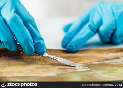 Professional painting conservator uses scalpel to carefully remove patches from an oil painting. Restoring Oil Painting