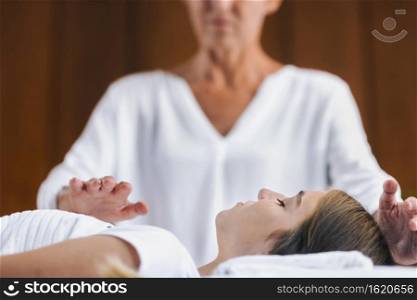 Professional Reiki healer doing Reiki treatment to young woman in health spa center. Healing and balancing heart and crown chakras