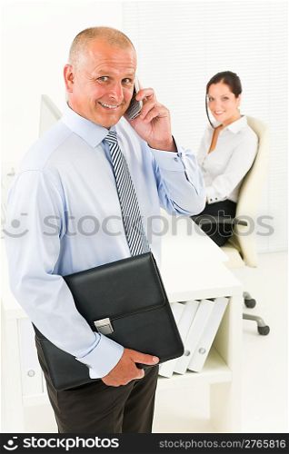 Professional senior businessman hold briefcase calling in office with secretary