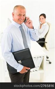 Professional senior businessman hold briefcase calling in office with secretary