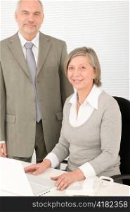 Professional senior businesswoman behind computer with male colleague