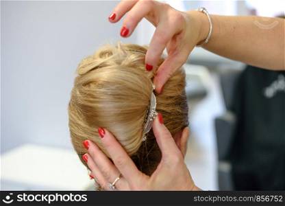 Professional services in the hairdressing salon - a young woman with blonde hair has made hairstyles for a wedding party.