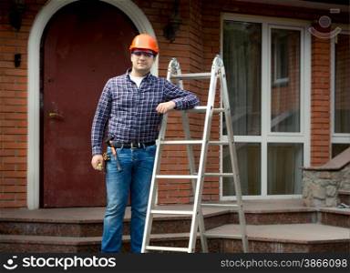 Professional worker posing with metal ladder against building house