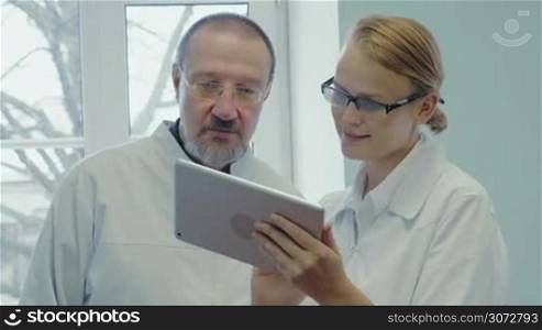 Professor and young female doctor having a conversation using digital tablet. They discussing something shown on pad and making an agreement