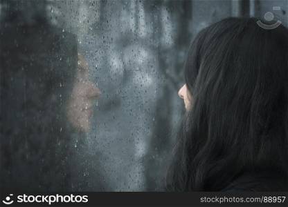 Profile image of a young brunette woman with closed eyes thinking in front of rainy window
