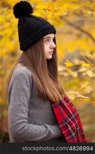 Profile of a pretty teenage girl wearing woolen hat with autumnal colours in the background